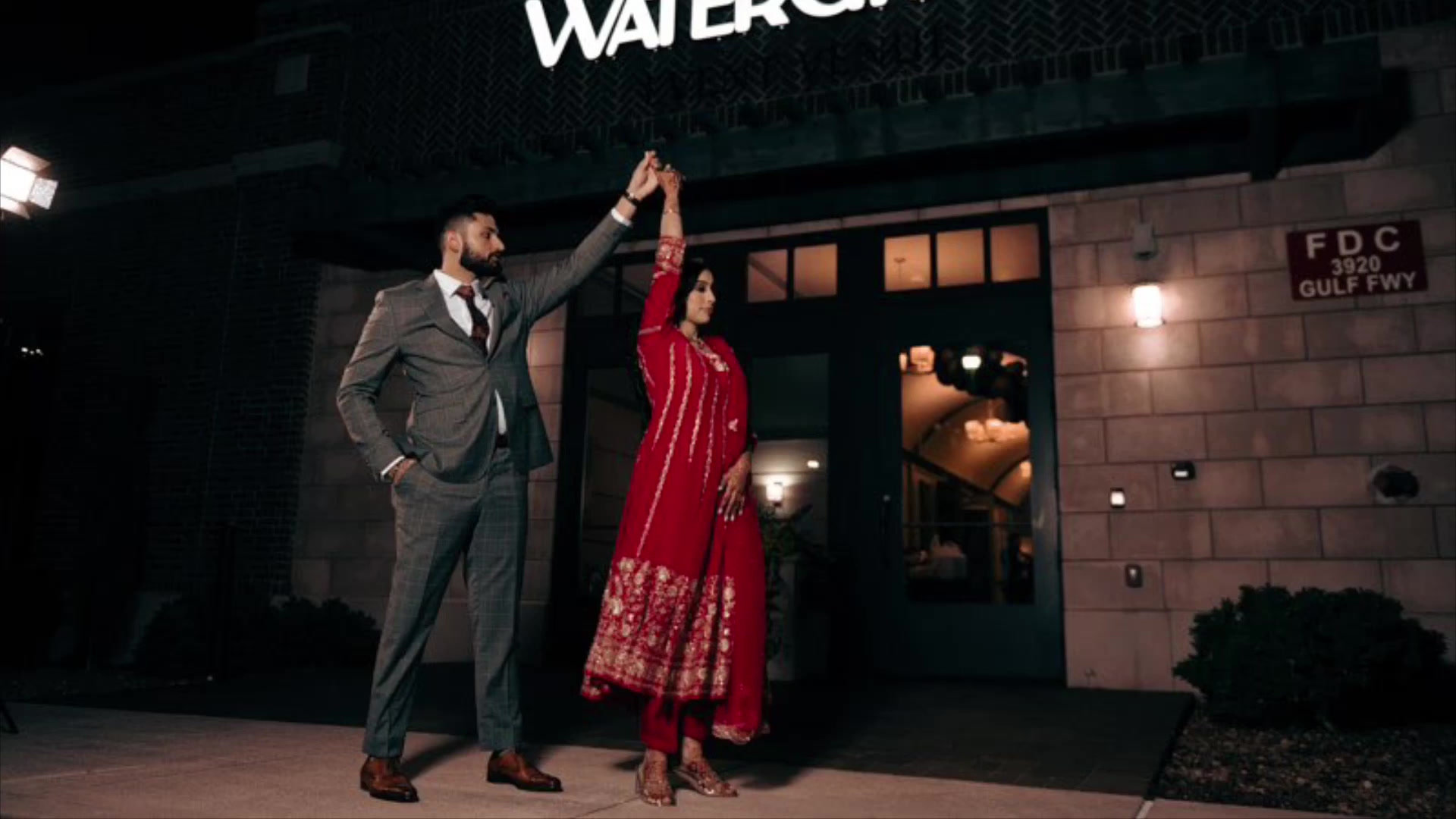 Still from a Kanha Arts wedding film: a groom twirling his bride in a red embroidered suit at night