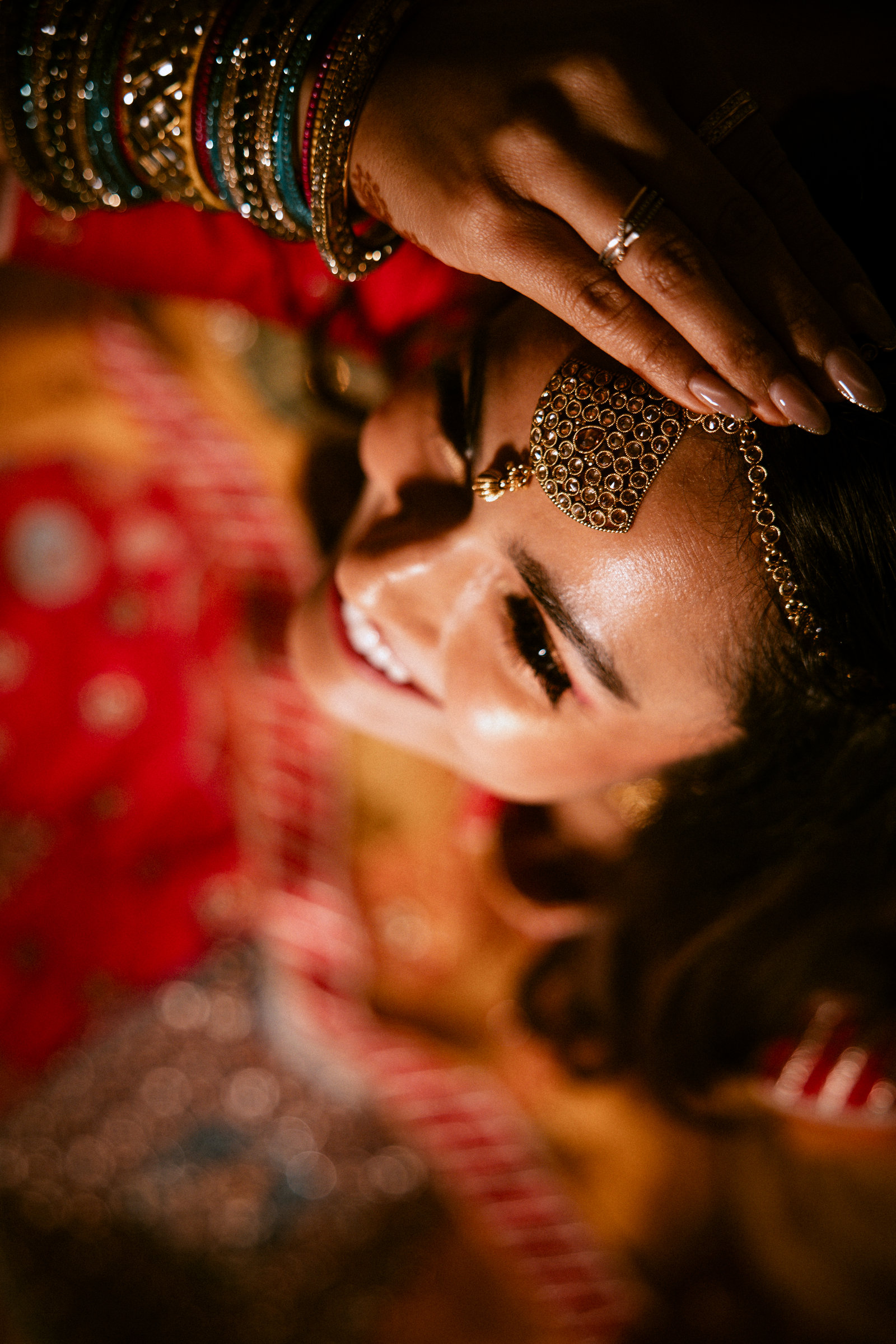 Close-up of a bride with mehndi-covered hands, bangles and red bridal jewellery