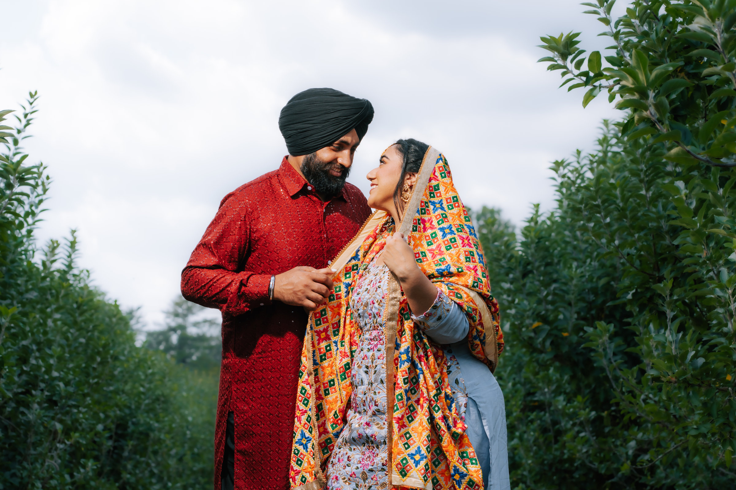 Punjabi couple outdoors, groom in a red kurta and turban, bride in a bright phulkari dupatta