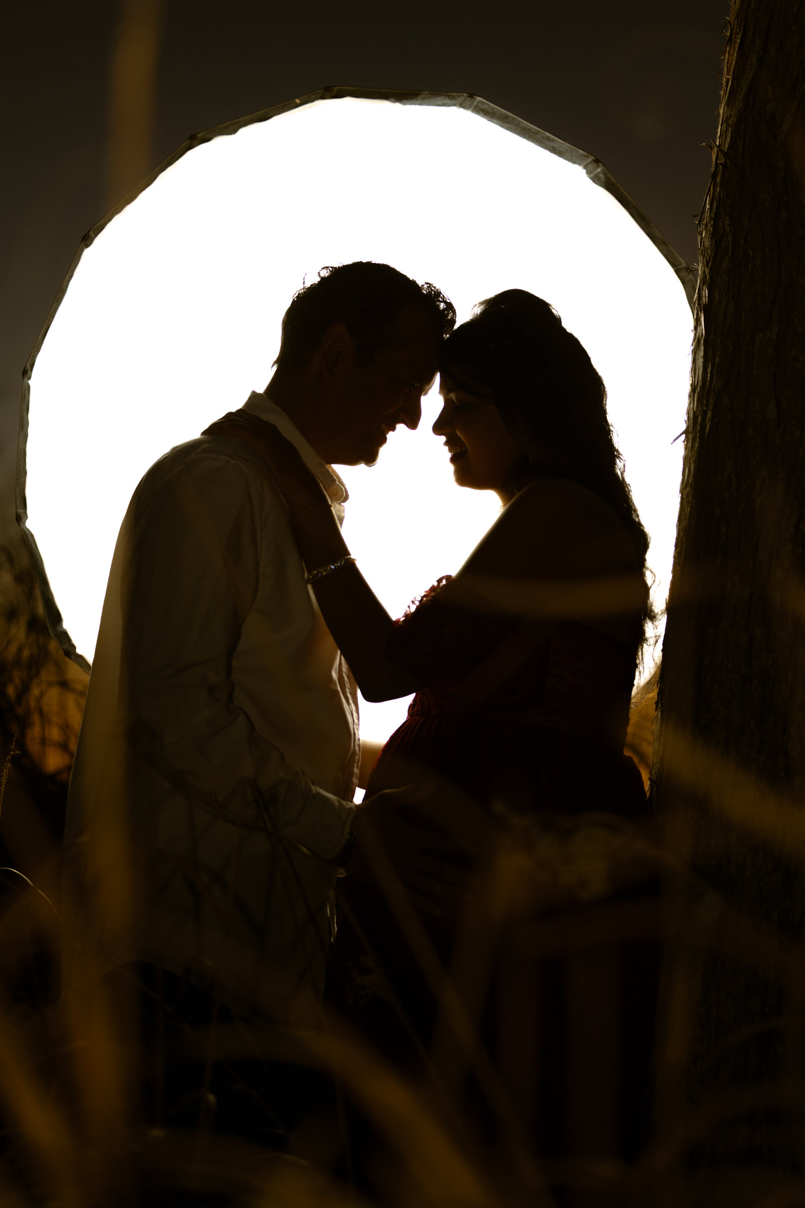Couple silhouetted forehead to forehead against a glowing circle of light at night