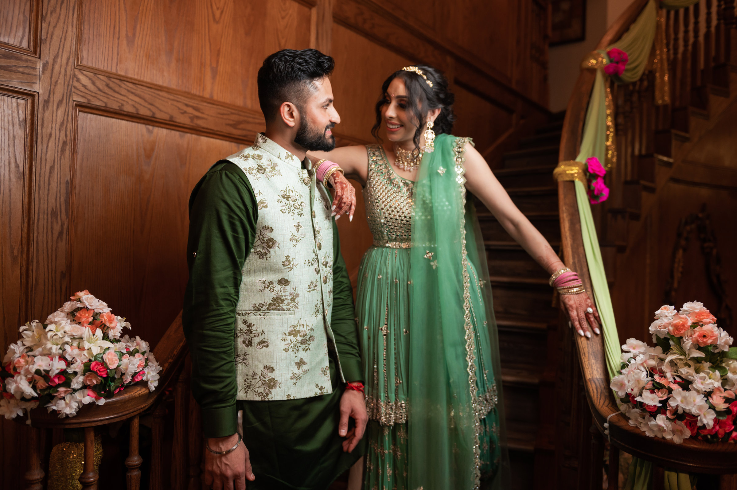 Couple in mint green outfits posing on a wooden staircase decorated with flowers