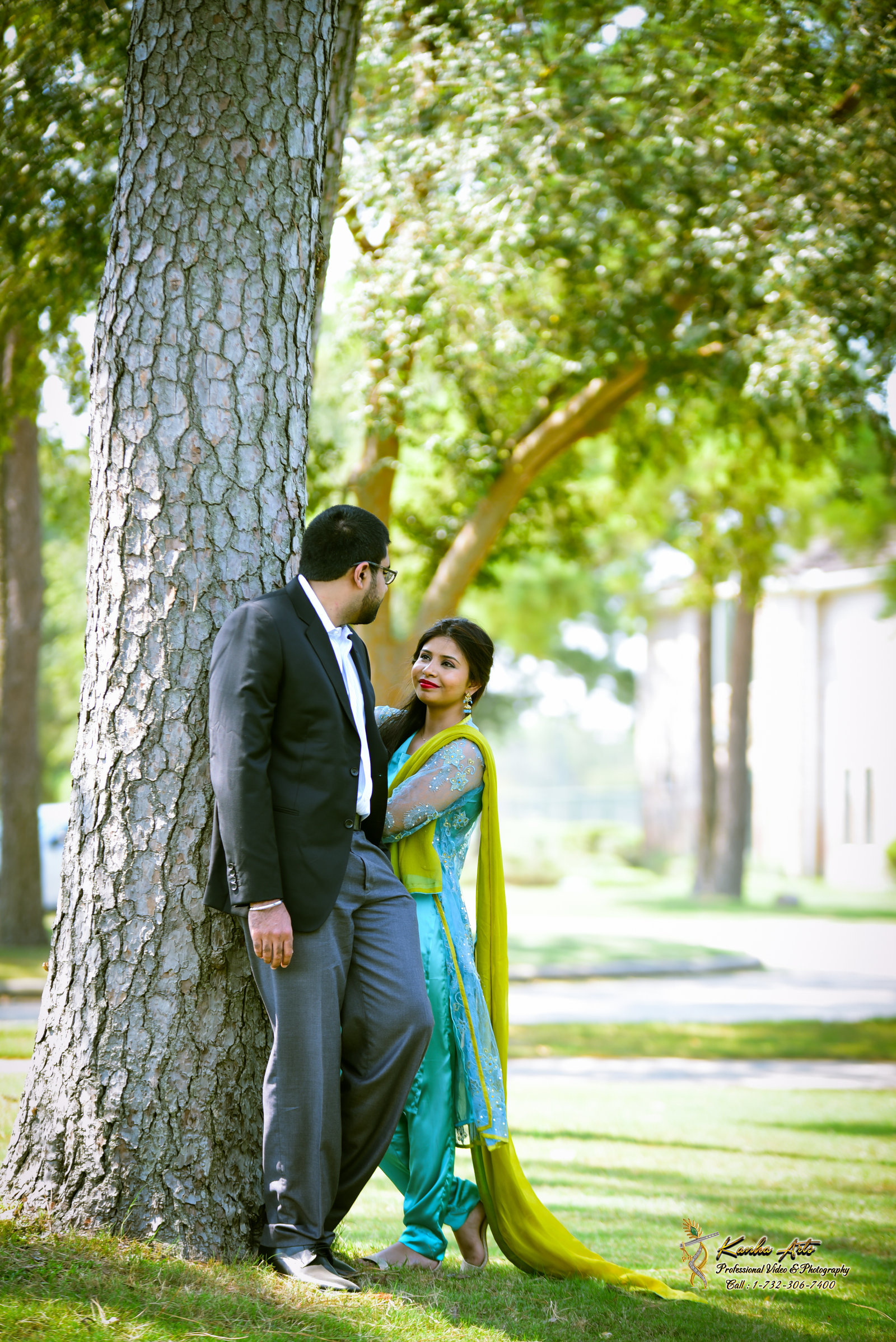 Couple leaning against a large tree in a green park, bride in a yellow and green suit